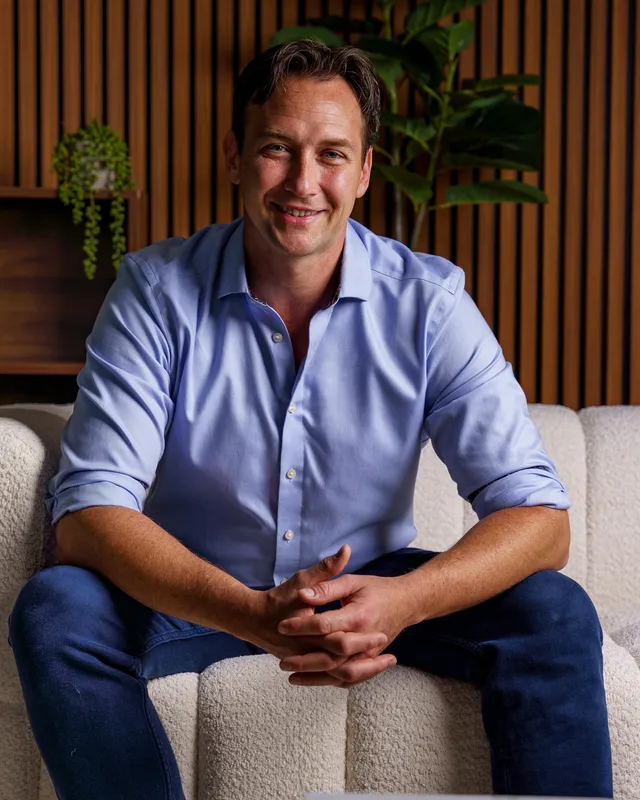 Jonathan Keen seated in front of a wood-panelled wall and plants.